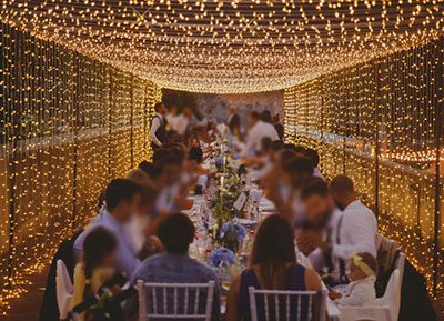 Immagine di un tunnel di luci con tavolata di pesone ad una cena di matrimonio